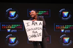 Aicha Evans, AnitaB.org Board Member and emcee of the GHC 17 Keynotes, stands on the main stage with her "I AM" statement: "I AM a conductor for change."
