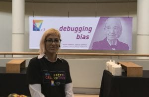 A GHC 17 worker stands in front of a poster of Grace Hopper that says, "Debugging bias"