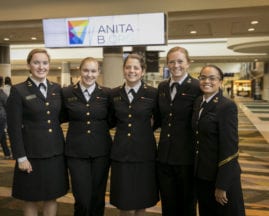 A group of young women dressed as Rear Admiral Grace Hopper stand near an "AnitaB.org" sign