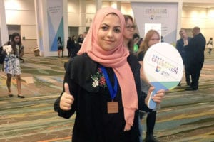 Mariam Nouh, 3rd place graduate winner of the ACM Student Research Competition, giving a thumbs up and holding a sign that says "Grace Hopper Celebration"