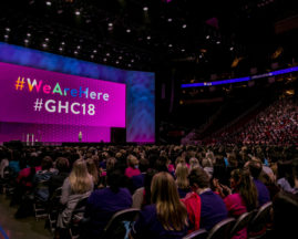 The screen above the stage at the GHC 18 Opening Keynote says "We Are Here #GHC18"
