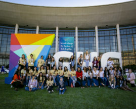 A large group of women attendees stand in front of the GHC and AnitaB.org logo display outside the OCCC at GHC 19