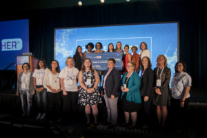 Dr. Sanna Gaspard holds her check on stage next to Brenda Darden Wilkerson and the judges after winning the 2019 AnitaB.org PitcHER competition
